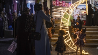 A Palestinian woman takes photos of her daughter next to a crescent moon-shaped decoration in a market