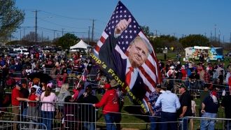 A large flag dons the likeness of former President Donald Trump as people gather at Waco Regional Airport.