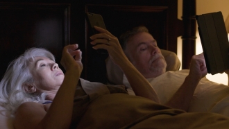 a couple in bed looking at their tablet and phone screens