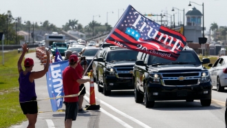 Supporters wave flags as a motorcade carrying former President Donald Trump returns to his Mar-a-Lago estate from the Trump.
