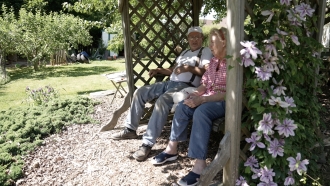 An elderly couple sits on a swing in their backyard