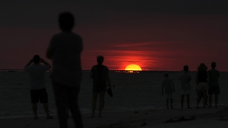 Residents and tourists watch a sunset over the ocean in Fort Myers Beach, Florida.