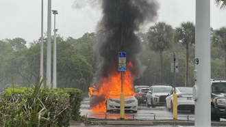 A car engulfed in flames in a parking lot