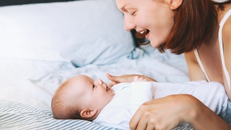 Woman smiles at a baby on the bed