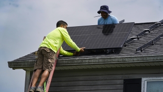 Two men installing solar panels on top of a house