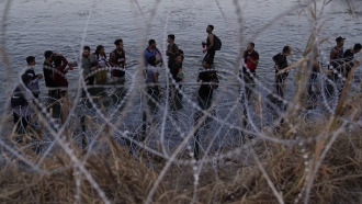Migrants wait to climb over concertina wire after they crossed the Rio Grande