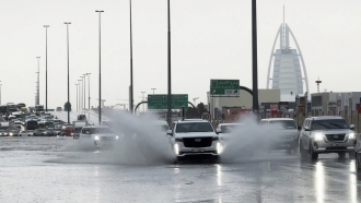 An SUV splashes through standing water on a road with the Burj Al Arab luxury hotel seen in the background in Dubai, UAE.