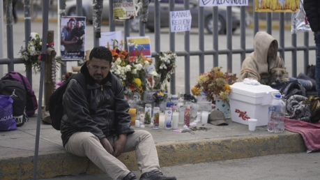A Venezuelan migrant sits on the sidewalk where an altar was created outside the detention center that caught fire.