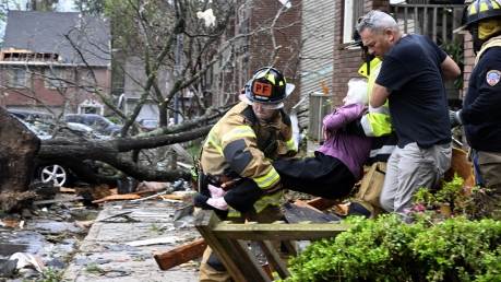 Firefighters carry a woman out of her condo after her complex was damaged by a tornado