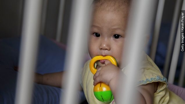 A young Chinese girl sits in a crib.