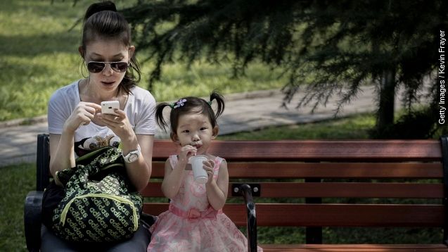A Chinese woman uses her smartphone as her daughter sits beside her on a park bench on September 10, 2014 in Beijing, China.