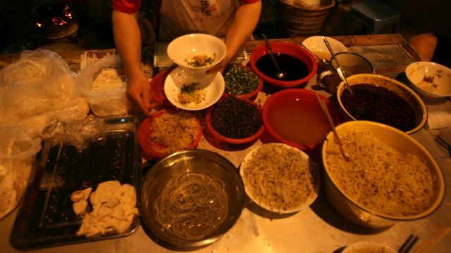 A vendor makes noodles for customers at a snack booth.