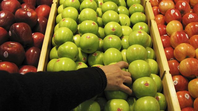 A woman reaching for apples at the grocery store.