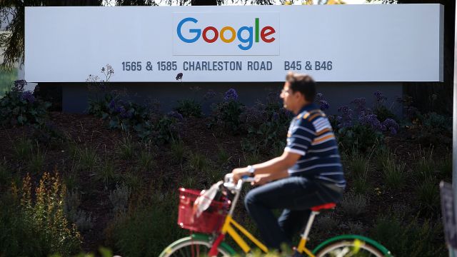 An employee at Google bikes past a sign.