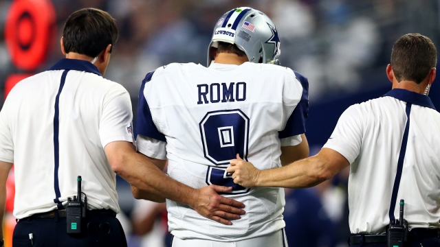 Tony Romo #9 of the Dallas Cowboys is led to the sidelines by team officials after being sacked by the Carolina Panthers in the third quarter at AT&T Stadium on November 26, 2015 in Arlington, Texas.