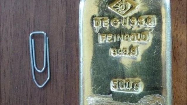 The $18,000 gold bar is pictured next to a paper clip for scale.