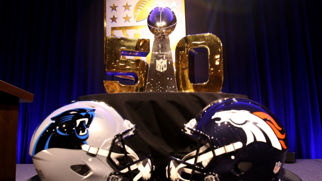 The Vince Lombardi Trophy in front of Carolina Panthers and Denver Broncos helmets