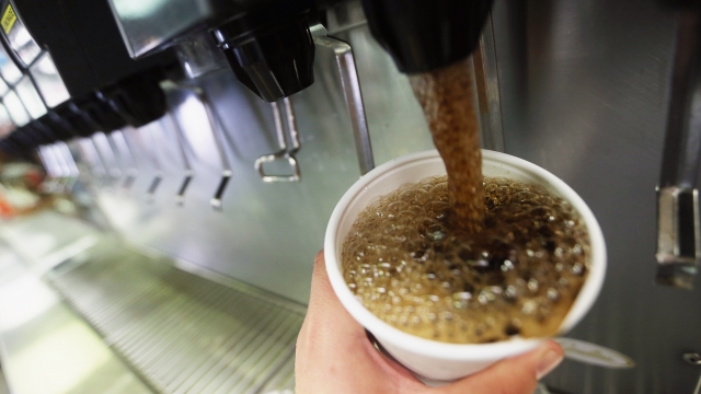 A person fills a cup with soda from a soda fountain.
