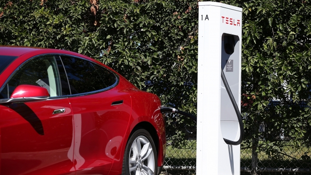 A Tesla car plugs into a supercharger.