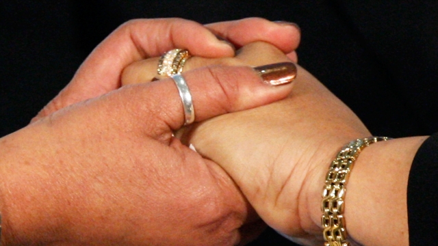 A lesbian couple holds hands during their marriage ceremony.