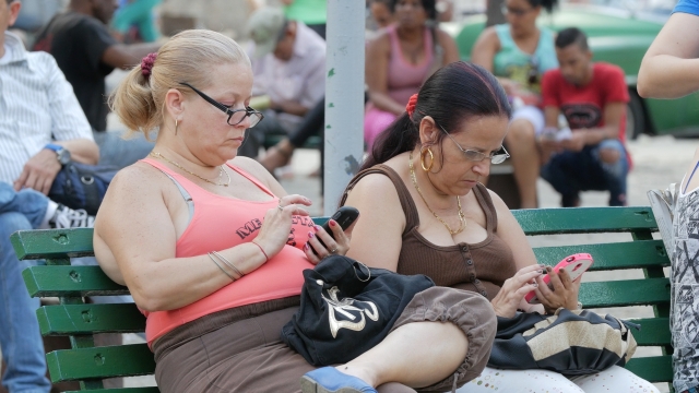 two Cuban women pay to access the internet in a public park