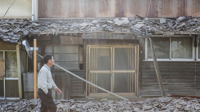 A local resident passes by collapsed house after an earthquake on April 15, 2016 in Mashiki, Kumamoto, Japan.
