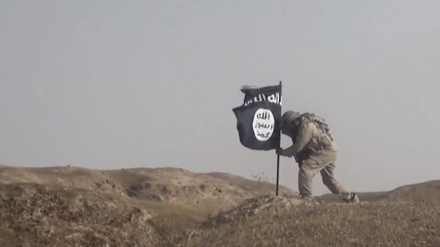 An ISIS fighter plants a flag.