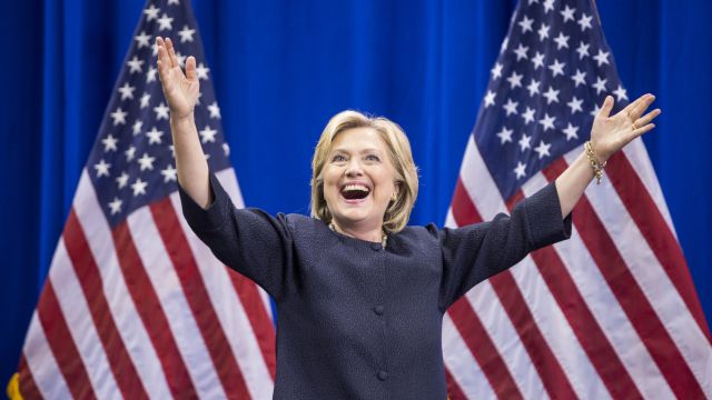 Democratic presidential candidate Hillary Clinton raises her arms stands on stage.