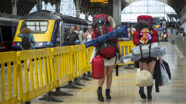 Two people with large camping backpacks walk through the train station in London.