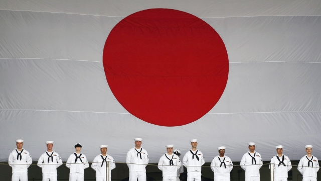 US navy soldiers line up in front of the national flag of Japan to see off the Kitty Hawk during a ceremony in Japan.