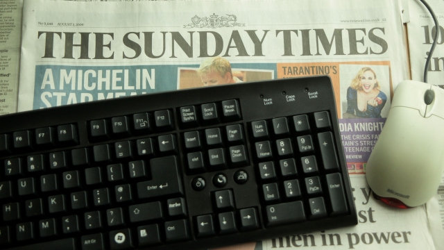 A newspaper rests under a computer keyboard and mouse