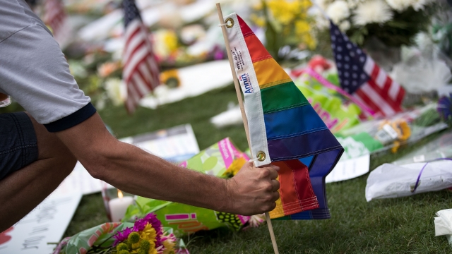 A man plants a pride flag at a makeshift memorial prior to an evening vigil for the victims of the Pulse Nightclub shootings.