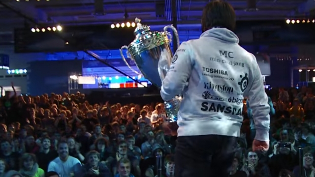 A gamer walks in front of a crowd with his trophy in hand.