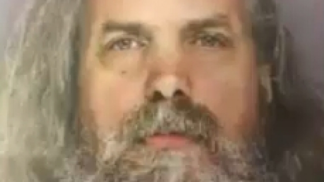A mugshot of Lee Kaplan who has long gray hair and a long gray beard.