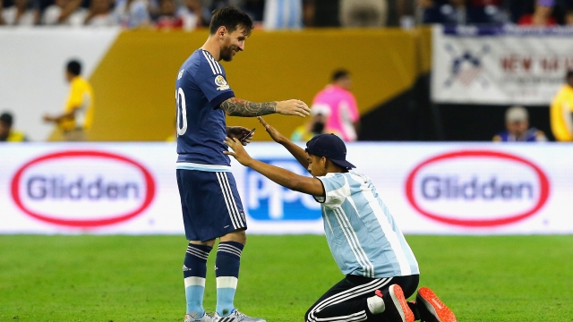 Lionel Messi #10 of Argentina interacts with a fan who ran onto the field prior to the start of the second half.