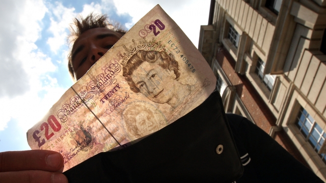 In this photo illustration, a man takes a 20-pound note from his wallet outside a bank in London, England.