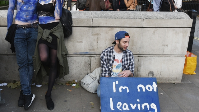 A young couple painted as EU flags and a man sitting with a sign that says "I'm not leaving"