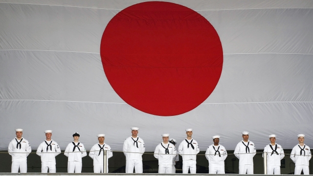 US navy soldiers line up in front of the national flag of Japan to see off the USS Kitty Hawk.