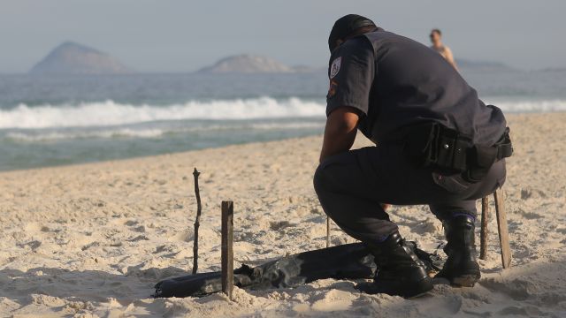 A police officer kneels over a body part covered in a plastic bag discovered on Copacabana Beach.