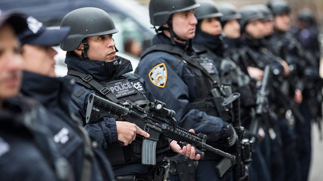 NYPD officers with the Strategic Response Group are in body armor and holding firearms while standing in row