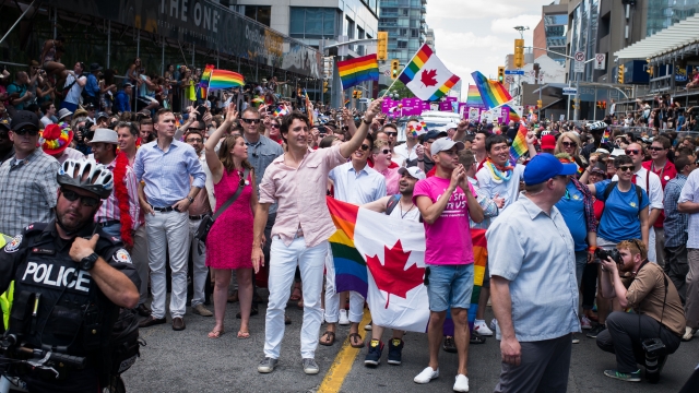 Justin Trudeau stands among parade marchers as he waves an LGBTQ Canadian flag.