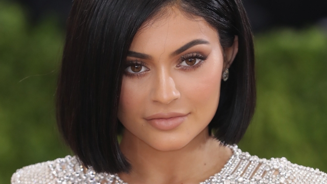 Kylie Jenner, with a short, dark bob haircut, wears and long-sleeve sparking silver dress.
