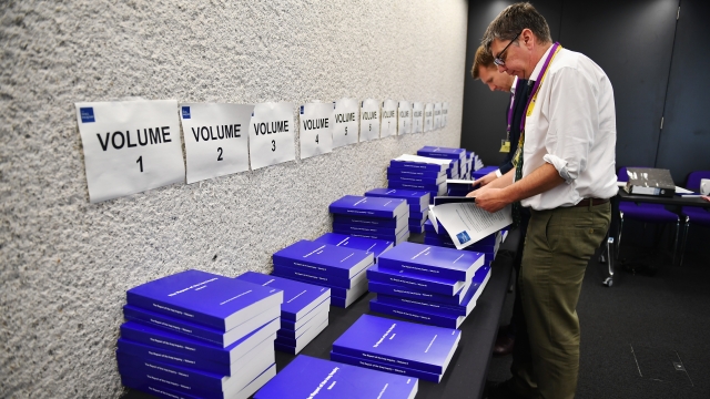 Two men stand in front of a table where many copies of the U.K's Iraq Inquiry have been placed.