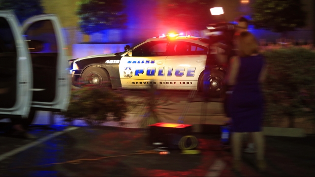 A Dallas police officer drives near the scene where eleven Dallas police officers were shot and five have now died.