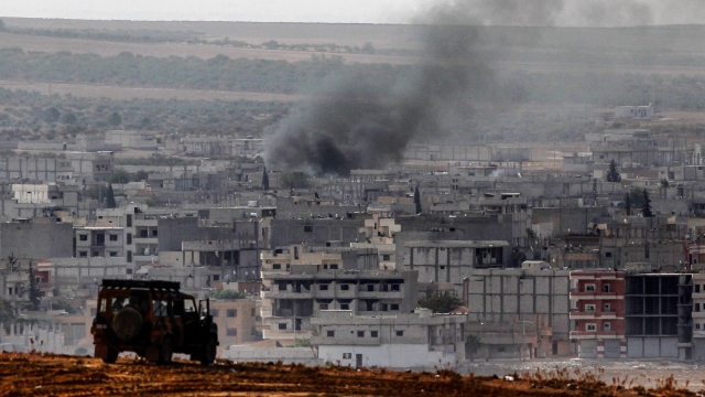 Turkish army vehicle overlooks a city where smoke rises after a US coalition airstrike.