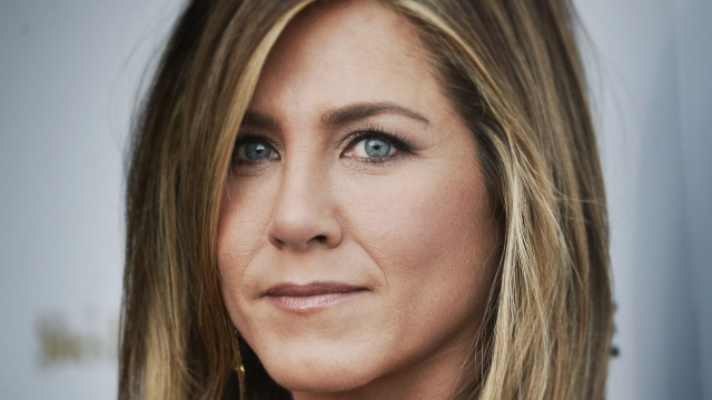 A close-up of Jennifer Aniston's face as she half-smiles wearing a black dress on a red carpet.