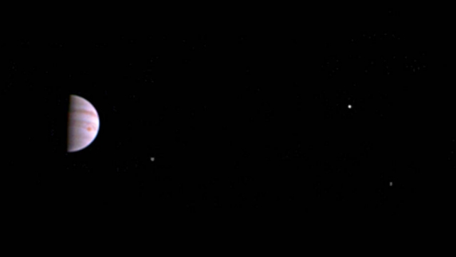 A photo of jupiter in the distance shows three of its large moons.