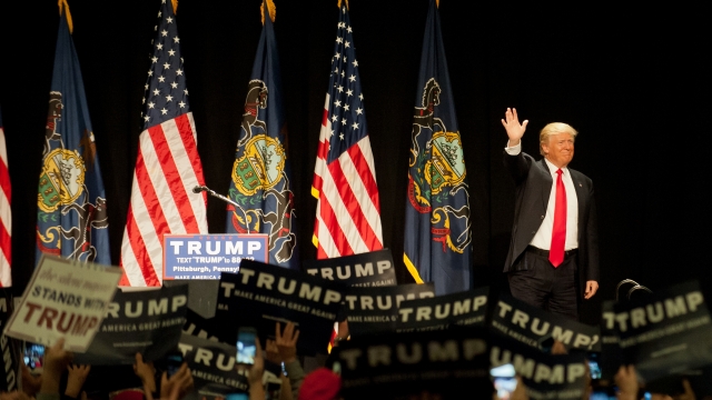 Republican presidential candidate Donald Trump stands by Pennsylvania and U.S. flags and waves to an audience at a rally.
