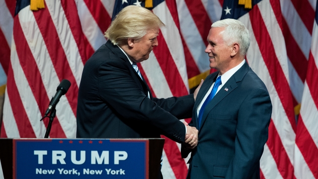 Donald Trump leaves the podium shaking Mike Pence's hand. Pence is wearing a navy suit and blue tie.