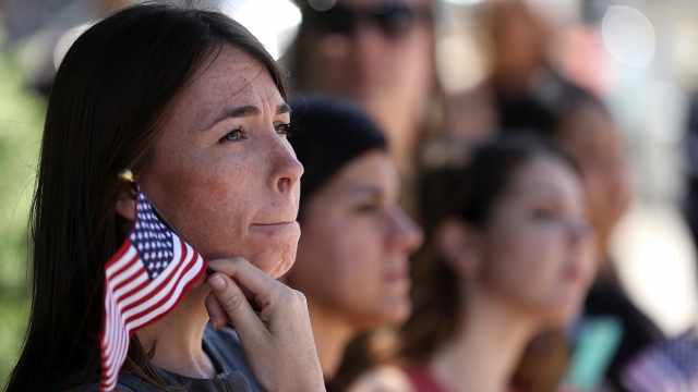 A woman with long brown hair holds a small American flag outside a funeral for an officer.